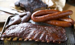Barbecue platter with glazed pork ribs, smoked sausage links, and smoked meat cuts at Hoots Smokehouse in Houston.